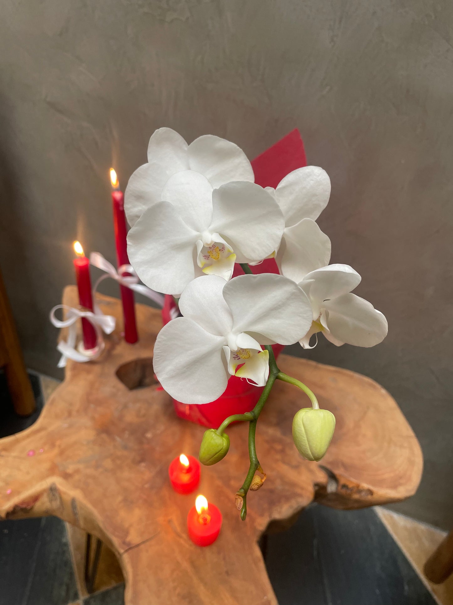 White orchid on a wooden surface with red candles in the background